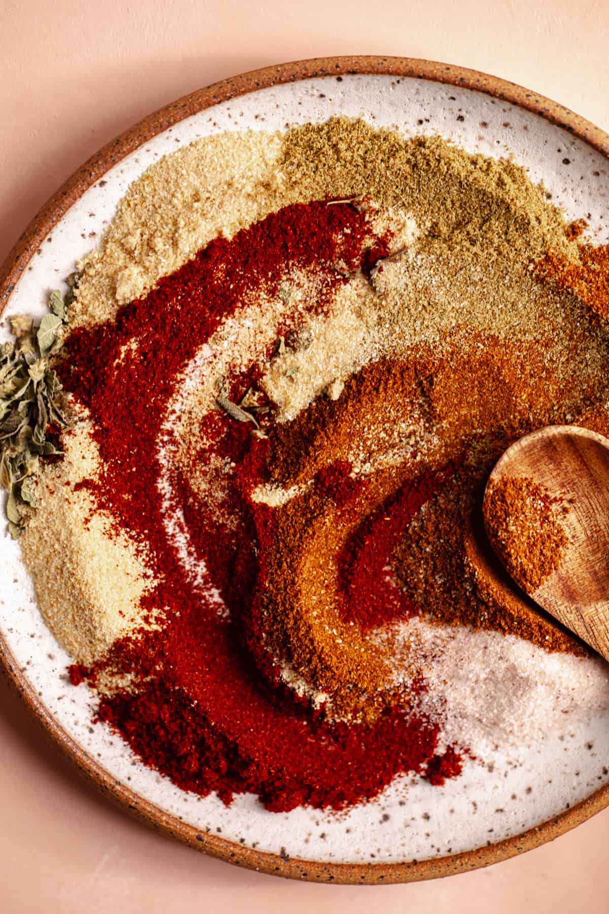 Spices being mixed together on a small plate with a wooden spoon.