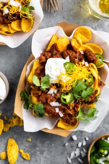 Boats of Frito pie served with sour cream, grated cheese, diced onion and slices of jalapeño.