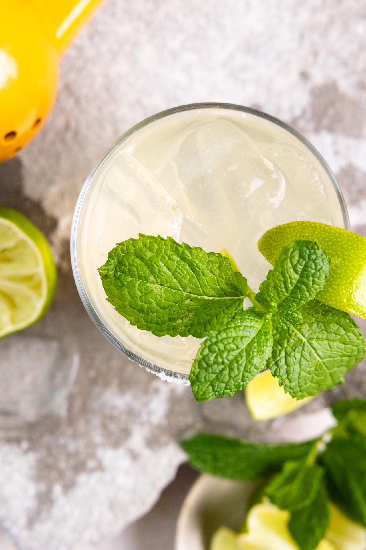 Overhead of a glass with margarita showing ice and mint leaf garnish.
