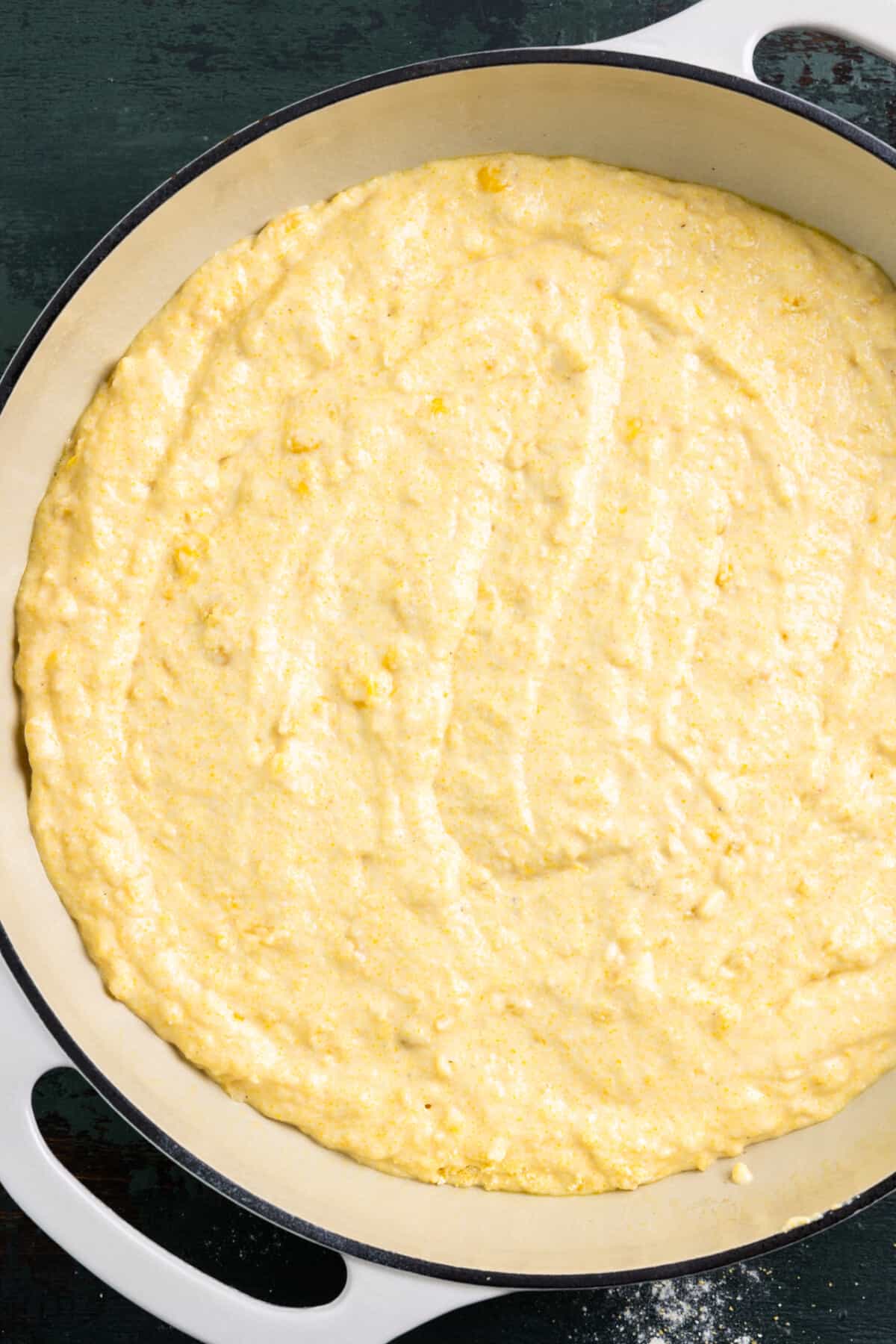 Cornbread batter spread out in a white baking dish. 