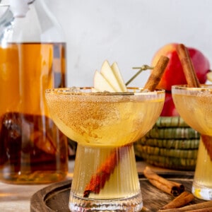 Glass filled with apple cider margarita garnished with slices of apples and cinnamon stick.