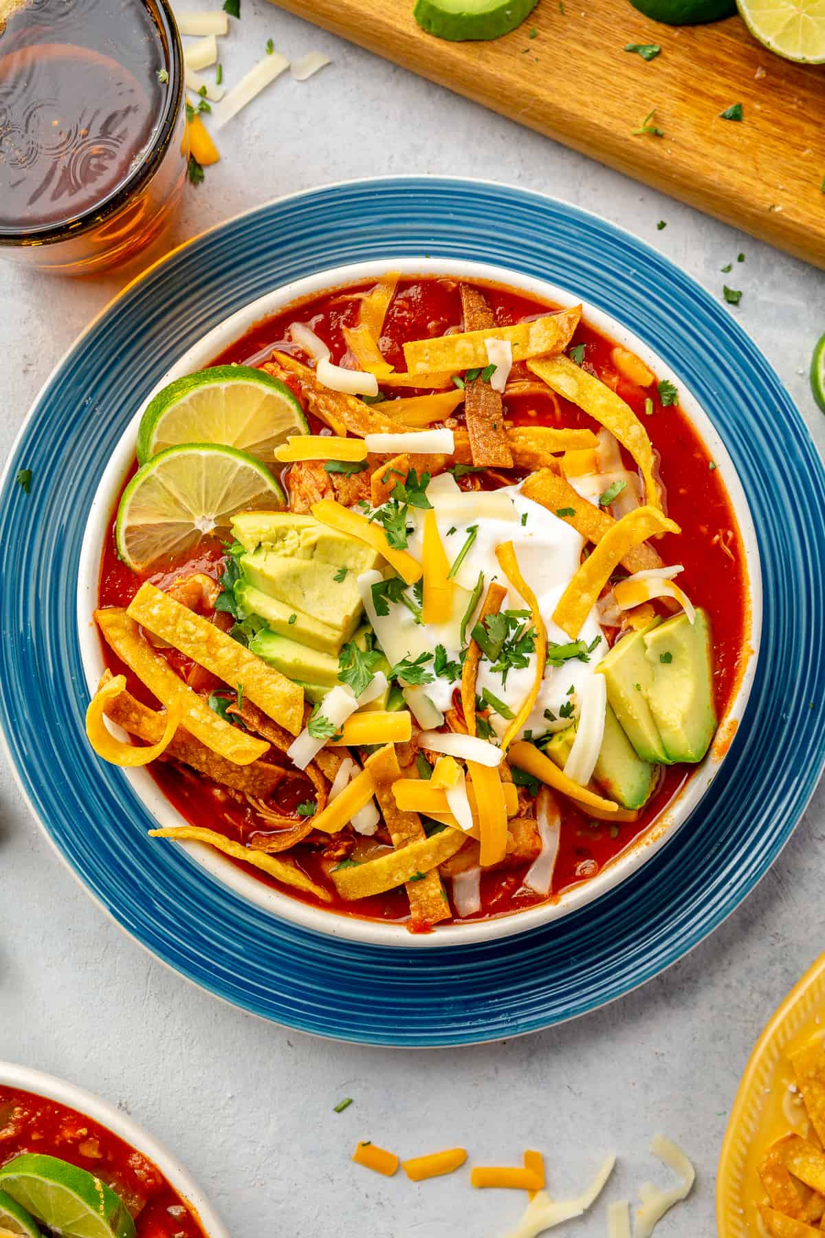 Bowl filled with chicken tortilla soup, topped with crispy tortilla strips, avocado, sour cream and slices of lime.