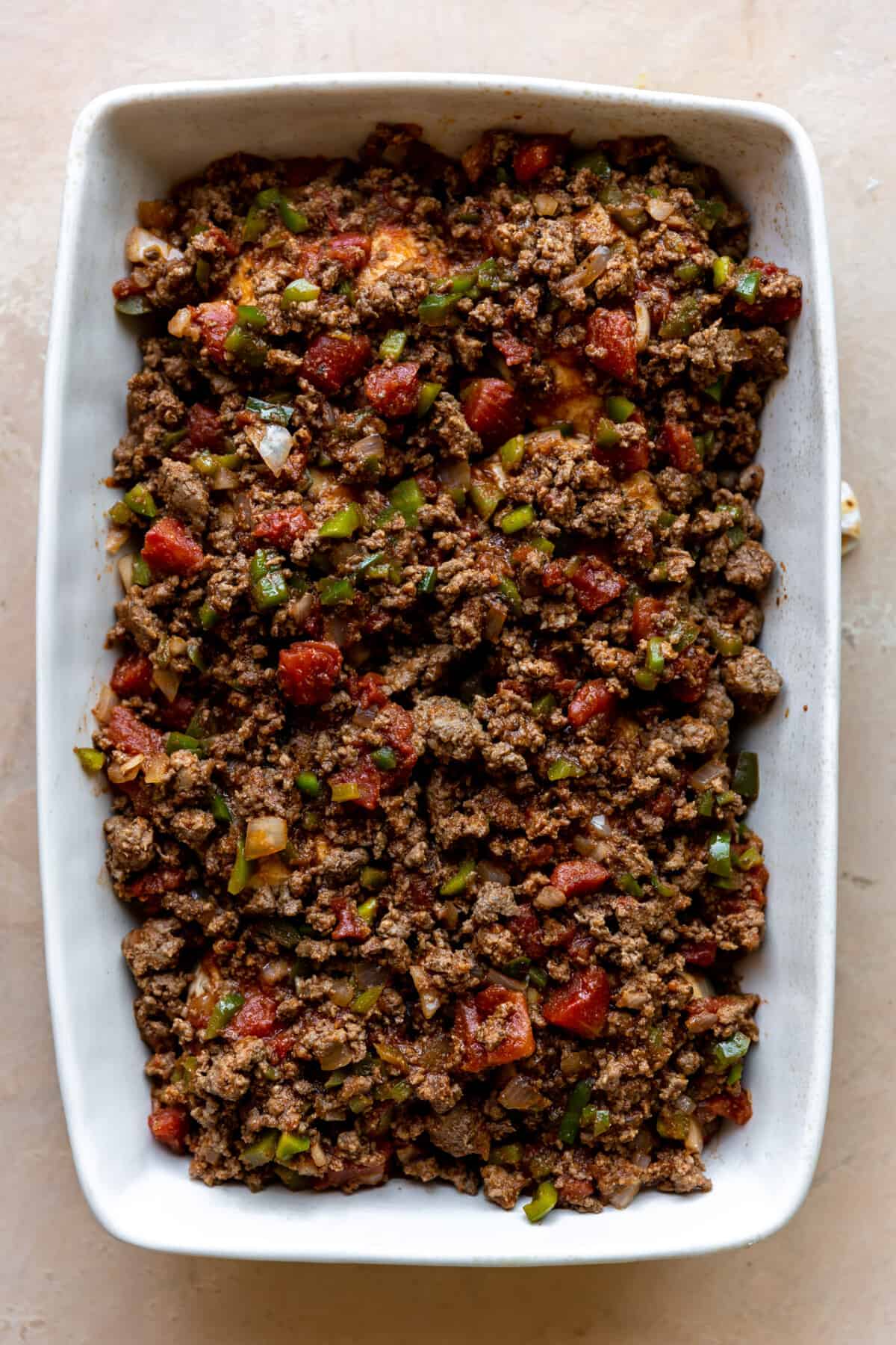 Ground beef mixture on top of baked biscuits in a baking dish to make a casserole.