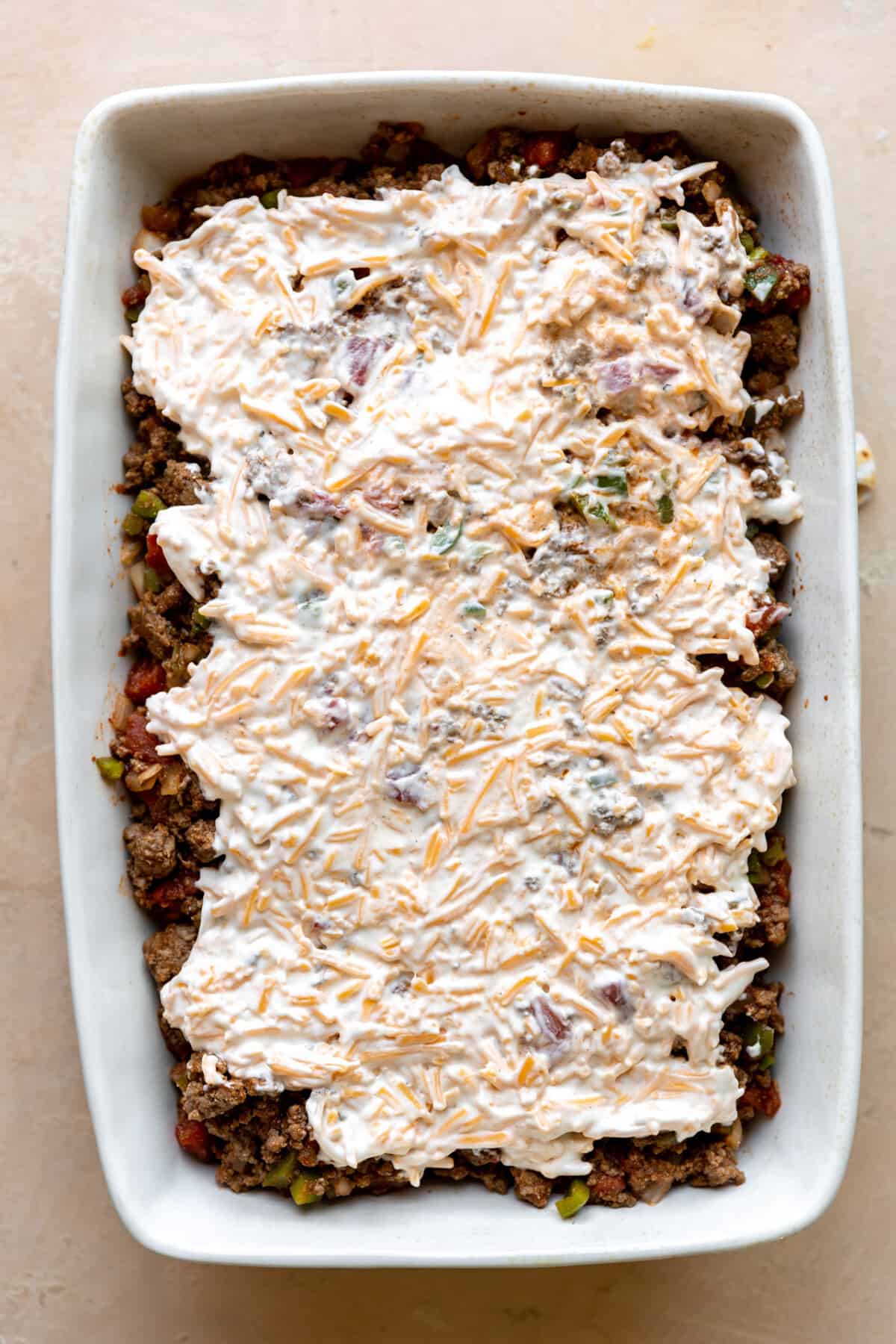 Cheese layer added on top of ground beef and biscuit in a white baking dish. 