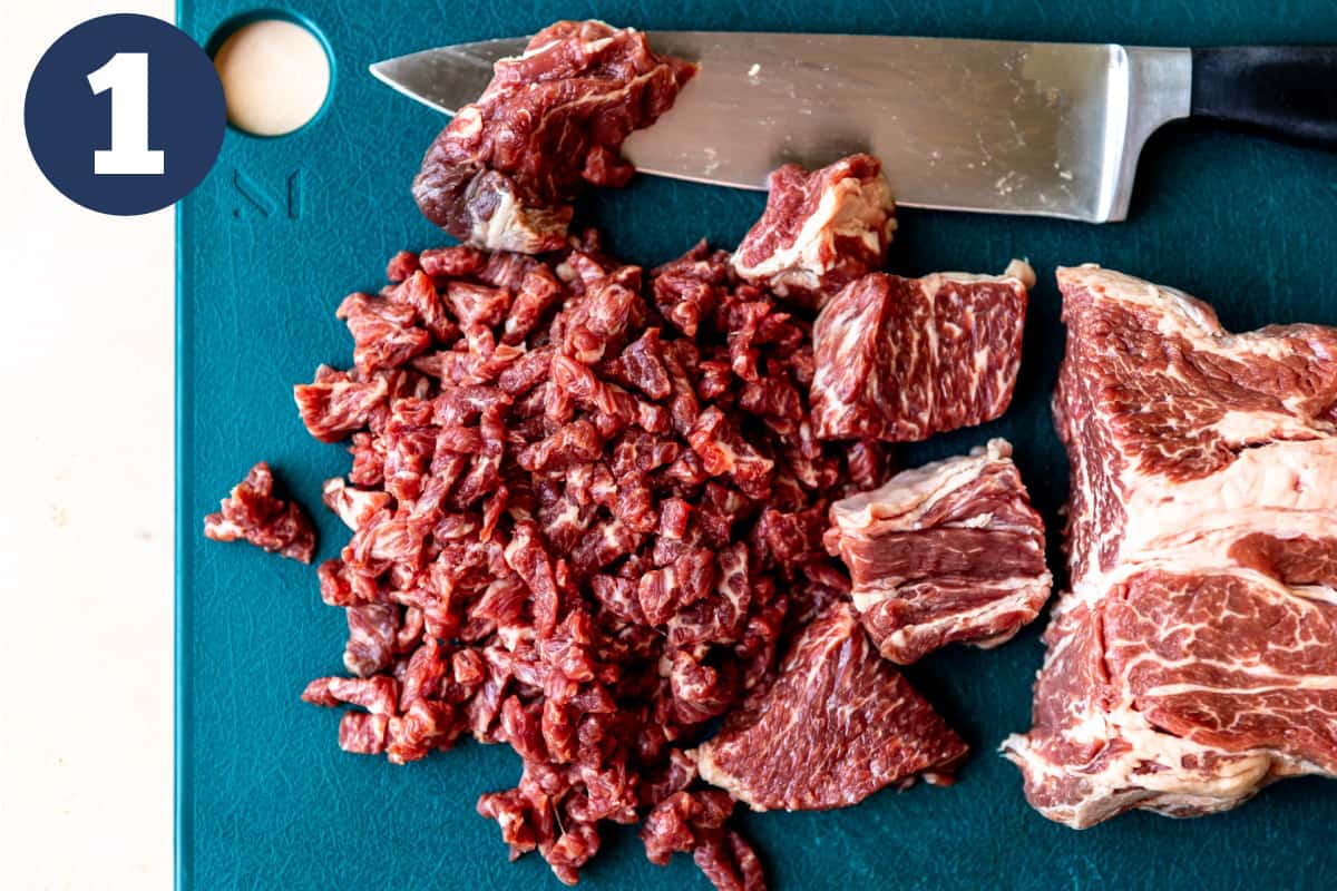 Cutting board with chuck roast being minced by a knife.