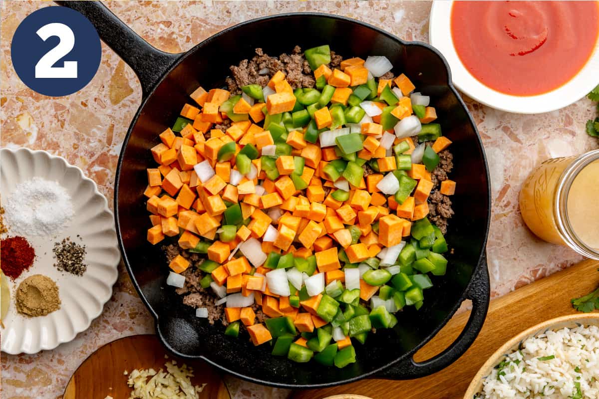 Diced sweet potato, onion and pepper added to cooked beef in a skillet. 