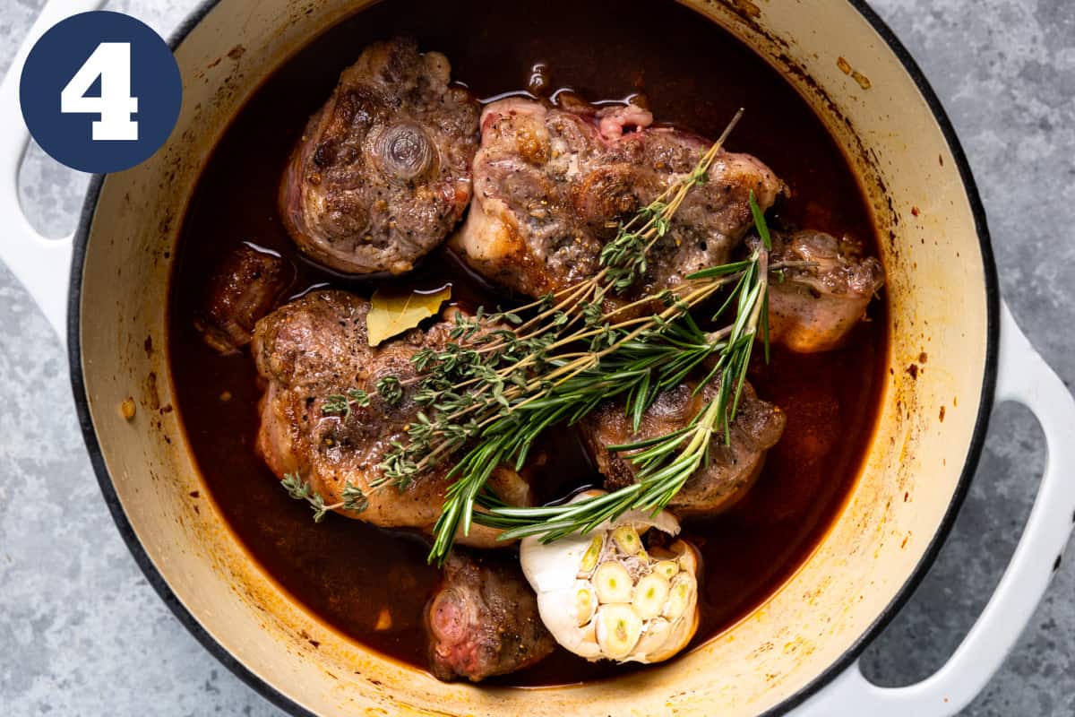 Oxtails in a dutch oven with broth, garlic, and herbs.