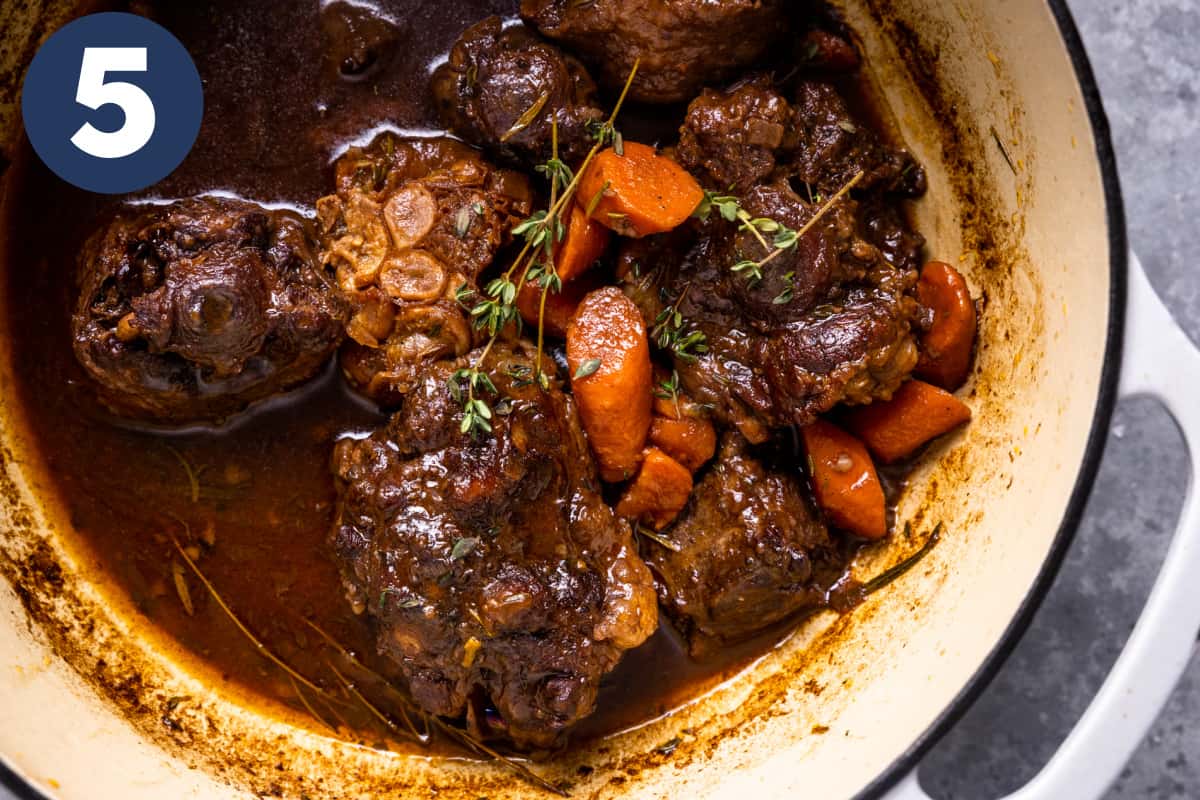 Braised oxtails in a dutch oven with carrots, garlic, and fresh herbs.