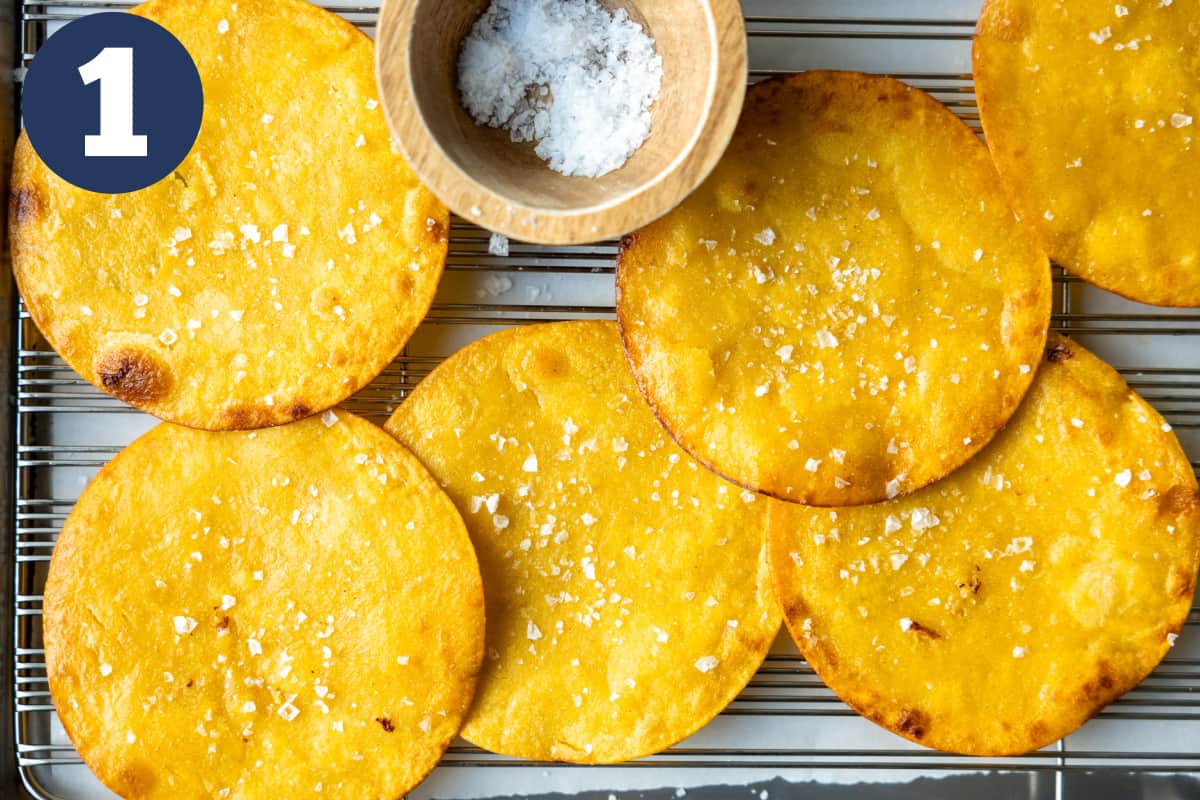 Fried tostadas on a wire rack with a bowl of salt. 