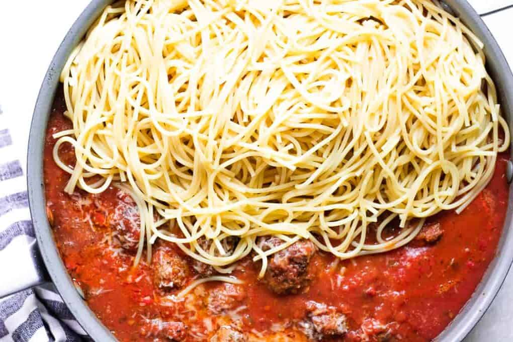Skillet filled with homemade spaghetti sauce and meatballs mixing in spaghetti noodles.