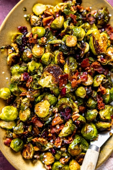 Roasted Brussels sprouts with bacon, pecans and dried cranberries on a gold serving plate.
