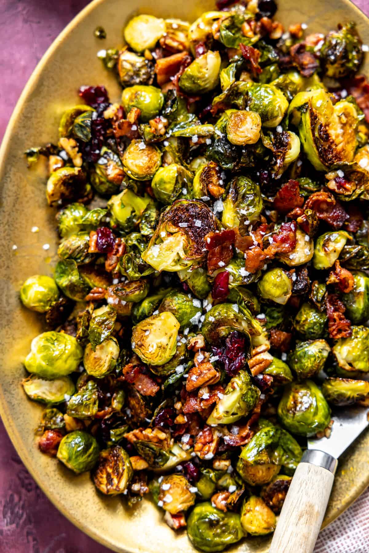 Roasted Brussels sprouts with bacon, pecans and dried cranberries on a gold serving plate. 