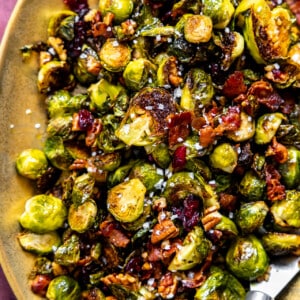 Roasted Brussels sprouts with bacon, pecans and dried cranberries on a gold serving plate.