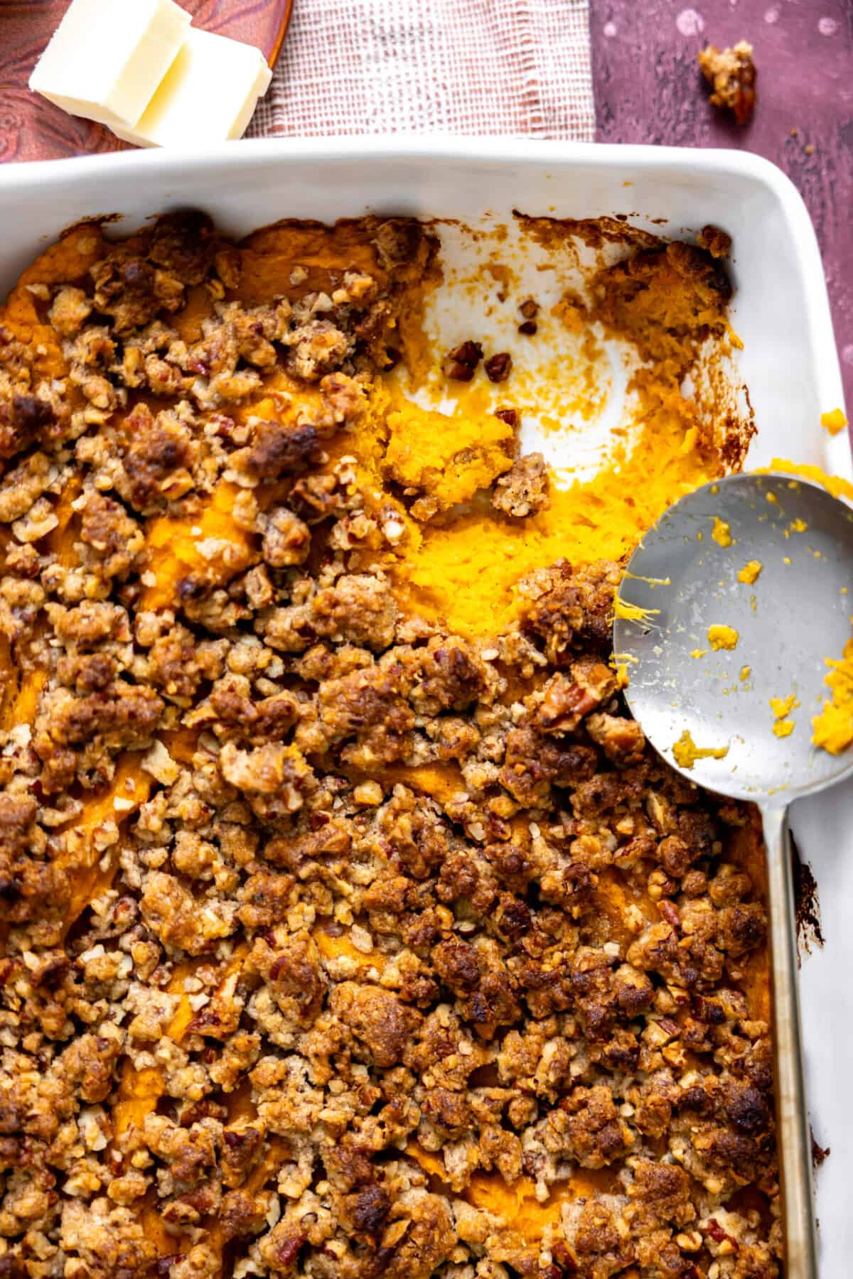 Spoon serving up sweet potato casserole with a pecan crumb topping. 
