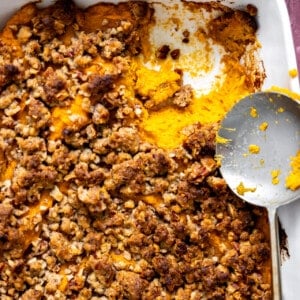 Spoon serving up sweet potato casserole with a pecan crumb topping.