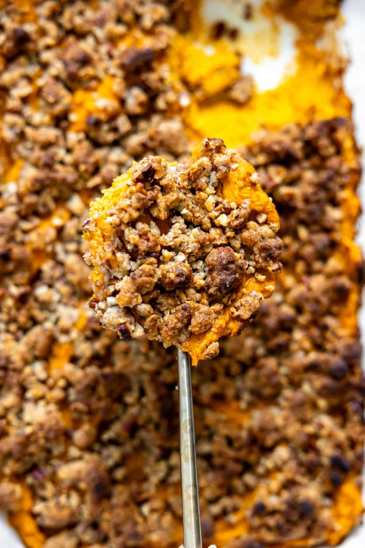 Spoon dishing up baked sweet potato casserole with crunchy pecan topping. 