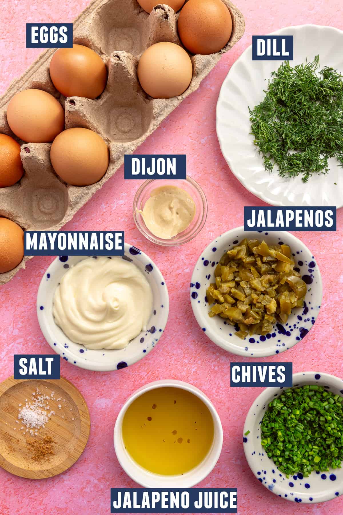Ingredients needed to make jalapeno deviled eggs laid on the counter: eggs, mayo, dijon, dill, chives, diced pickled jalapeño, and jalapeno juice. 