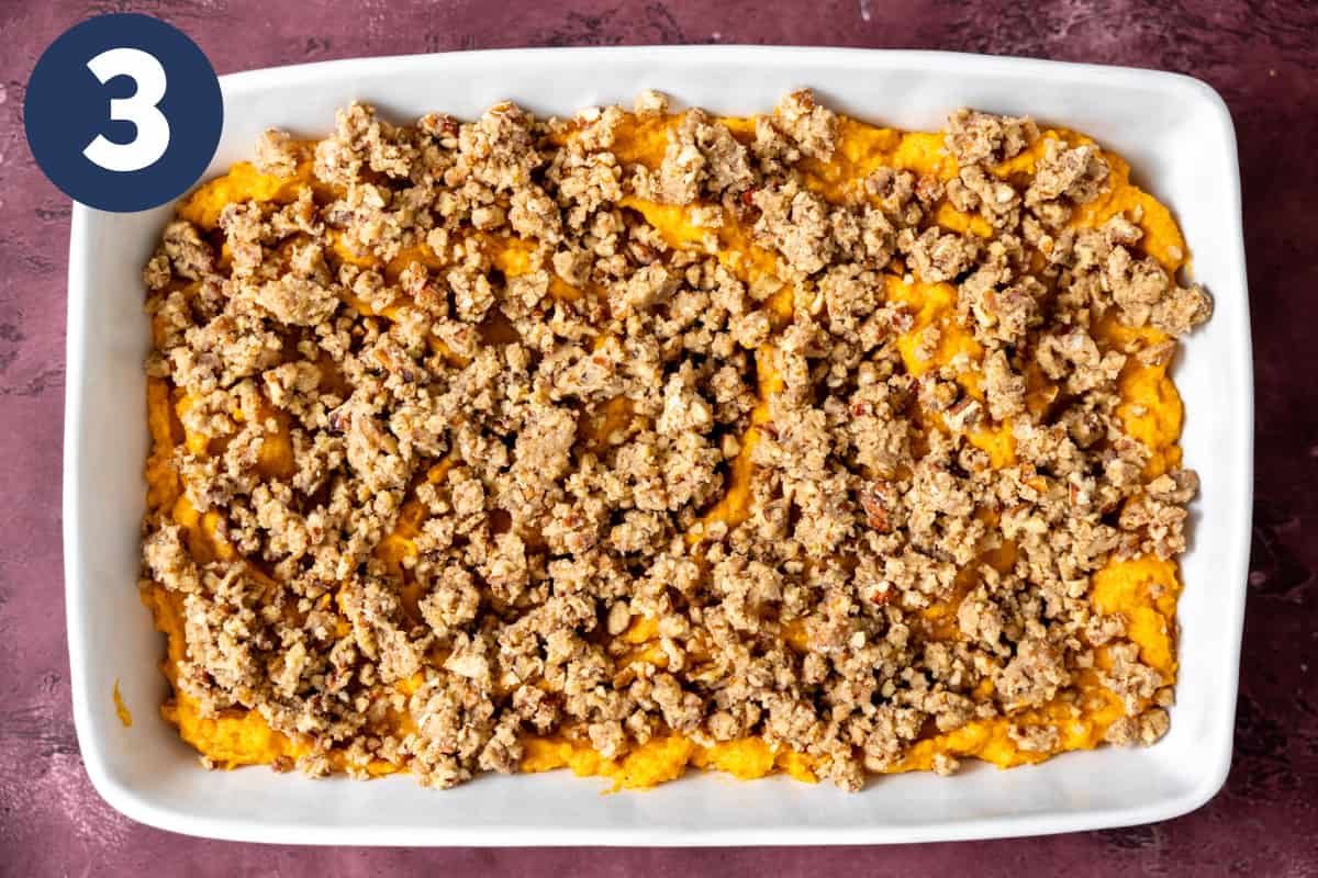 Pecan crumble topping on top of pureed sweet potato in a baking dish. 