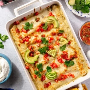 Casserole dish with breakfast enchiladas topped with diced tomato, avocado and cilantro.