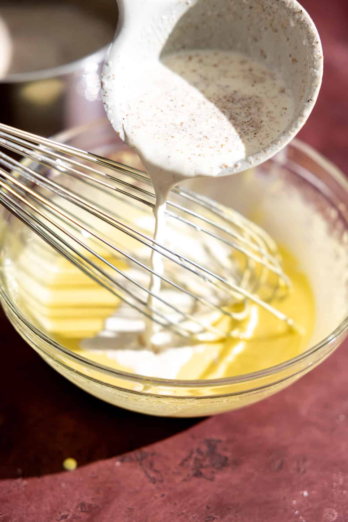 Warm cream being poured into egg yolks to temper.