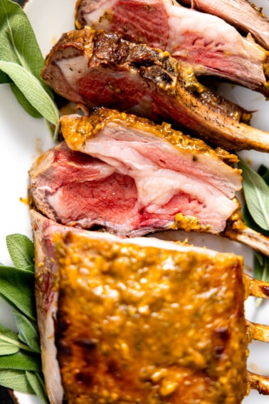 Sliced rack of lamb served on a white plate with sage.