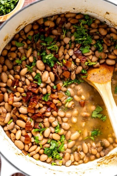 Pot filled with charro beans topped with bacon and cilantro.