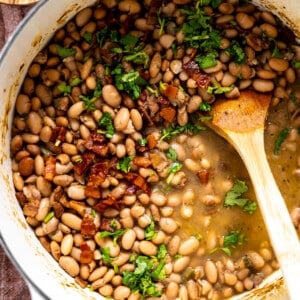 Pot of charro beans topped with cilantro and crispy bacon.