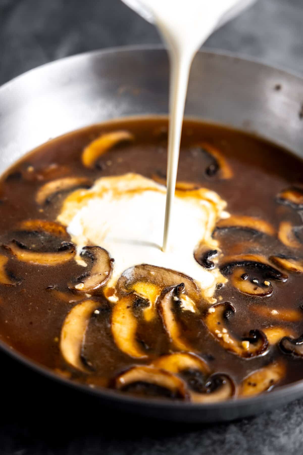 Cream pouring into skillet with a mushroom sauce.