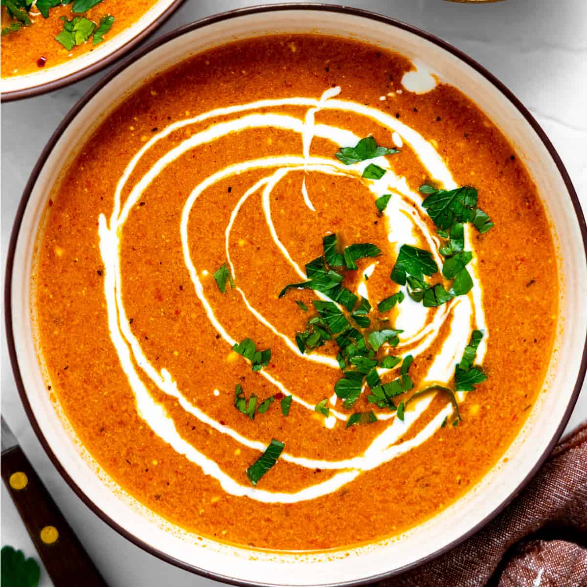 Bowl of red peppers soup with a swirl of sour cream. 