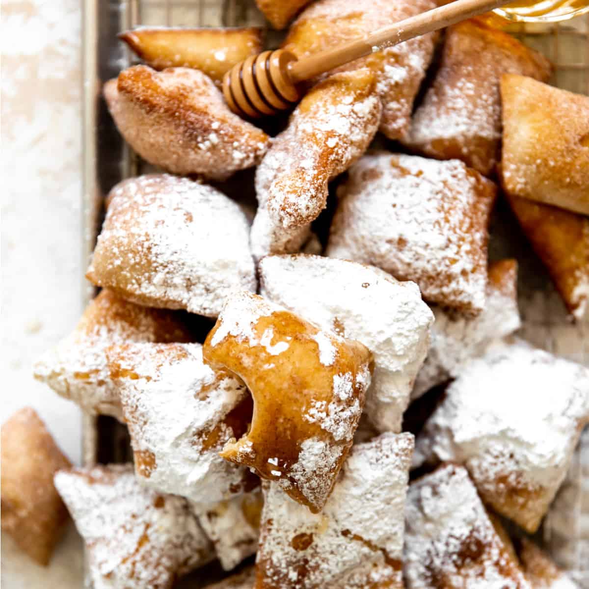 Tray filled with sopapillas coated with powdered sugar and drizzled with honey.