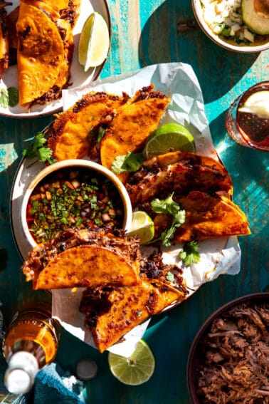 Birria Tacos served on a plate with a bowl of consommรฉ.