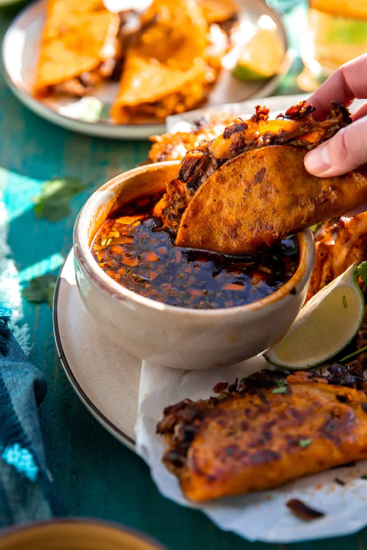 Birria taco dunking into a bowl of consommé.