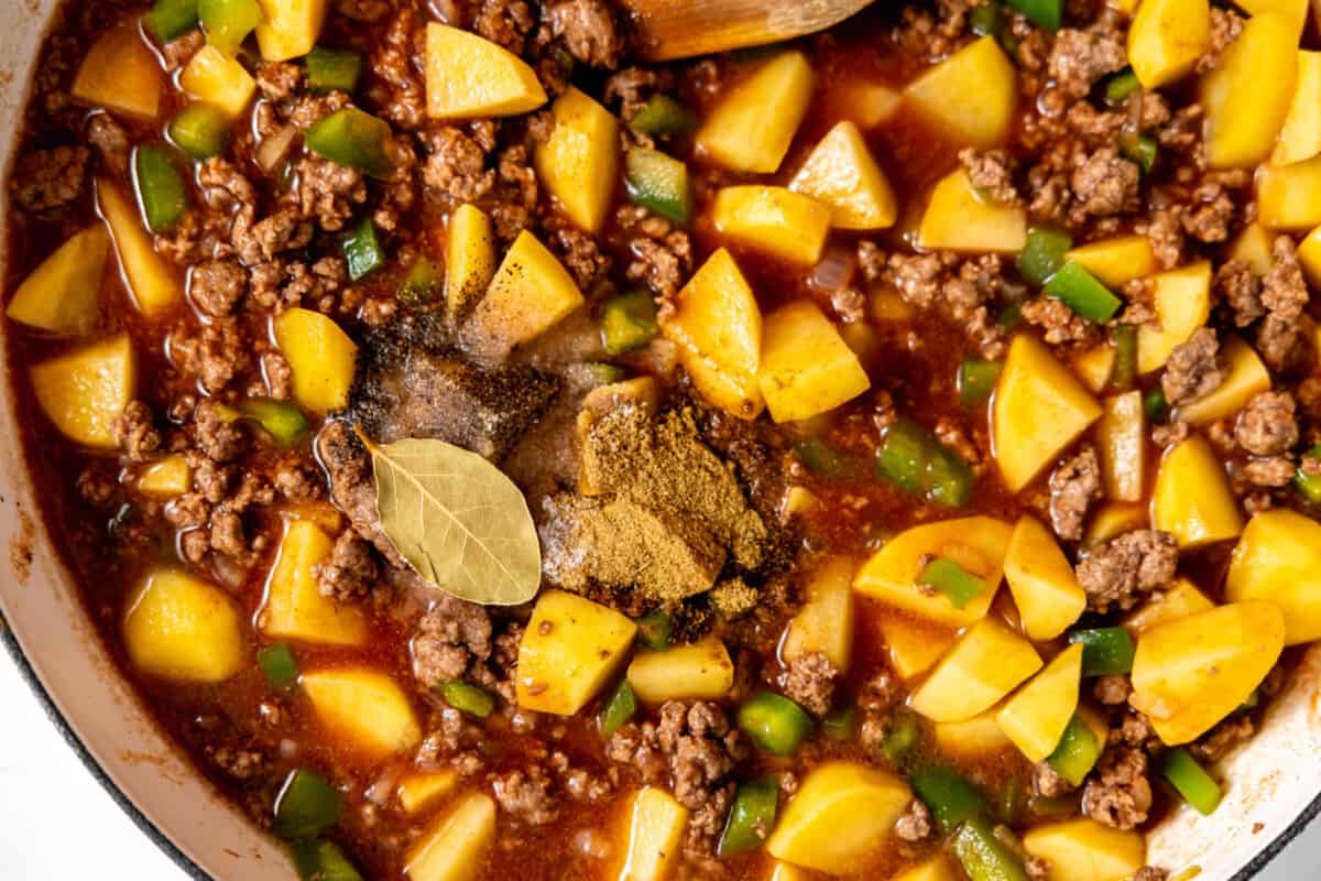 Mexican picadillo with ground beef and potatoes in a skillet topped with bay leaves. 