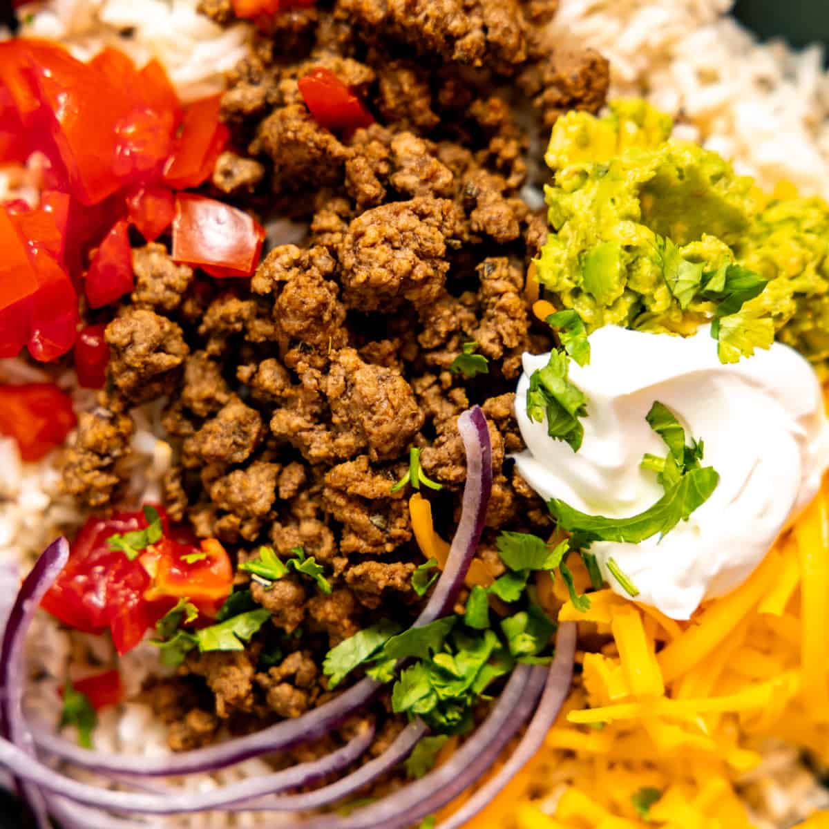 Bowl of rice, taco meat and taco toppings. 