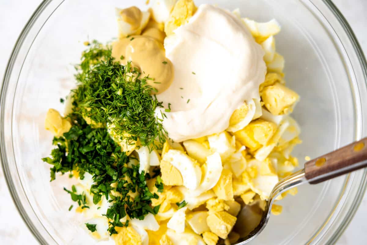 Bowl with chopped hard boiled eggs, mayo, mustard and fresh herbs for egg salad. 