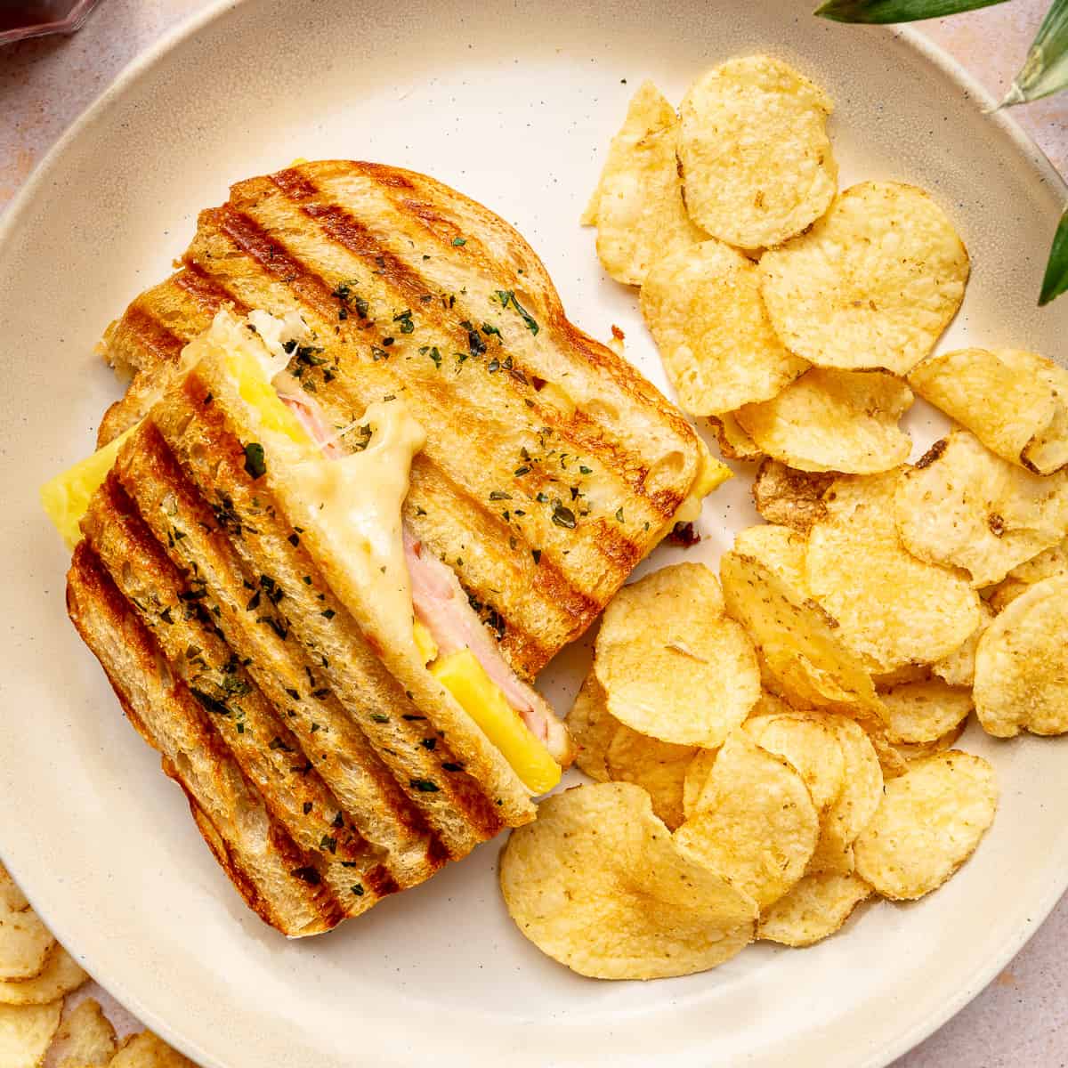 Hawaiian grilled cheese sandwich served with potato chips on a plate.