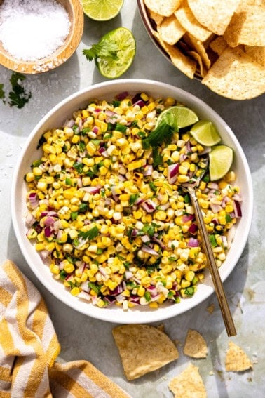 Bowl of roasted corn salsa with lime wedges.