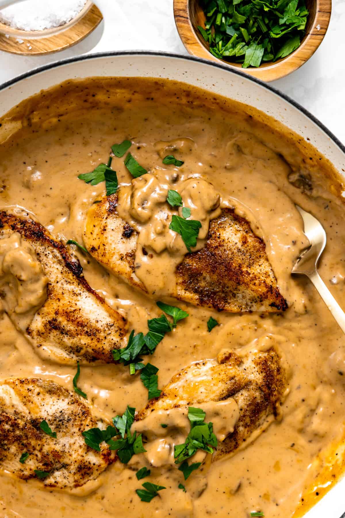Chicken Breasts smothered in a creamy mushroom sauce topped with herbs being served with a spoon.