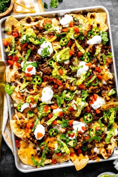Sheet pan nachos with ground beef topped with sour cream and guacamole.
