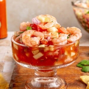 Mexican shrimp cocktail served in a glass cocktail glass on a wood board.