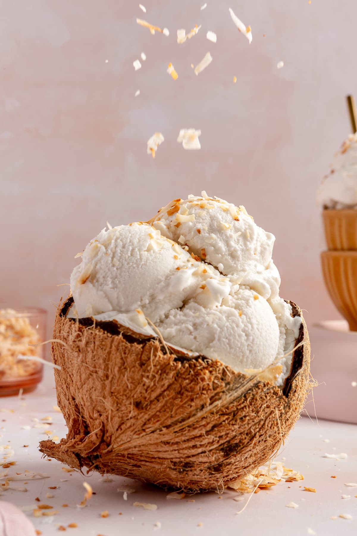 Half a coconut filled with scoops of coconut sorbet with toasted coconut being sprinkled on top.