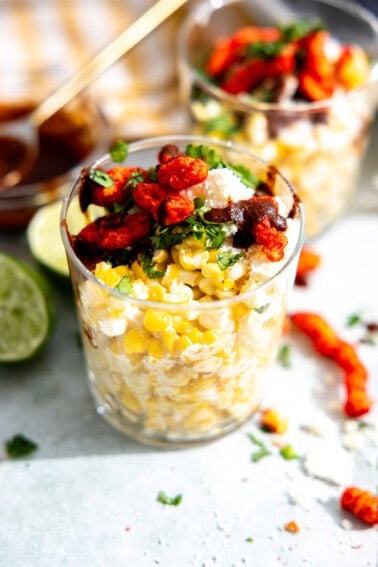 Esquites, Mexican street corn in a cup, topped with queso fresco, hot Cheetos, fresh cilantro and a chile sauce.