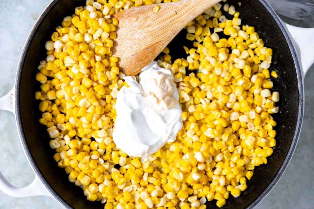 Adding mayo and sour cream to corn in a skillet to make street corn.