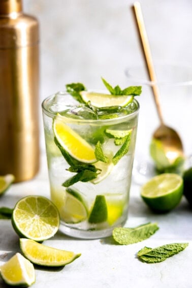 Glass with mojito with fresh mint and lime wedges.