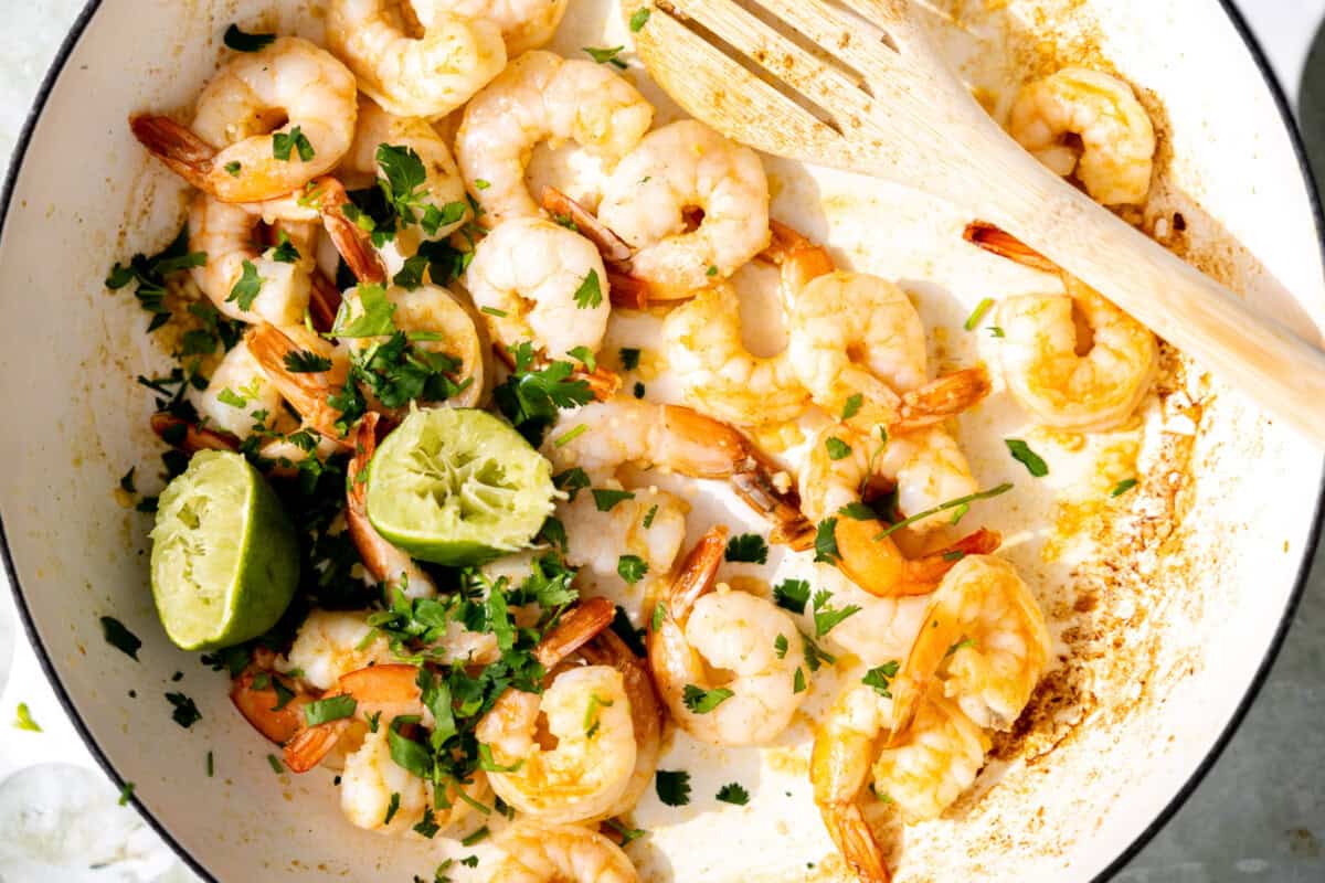 Cooked shrimp in a skillet with lime juice and cilantro added. 