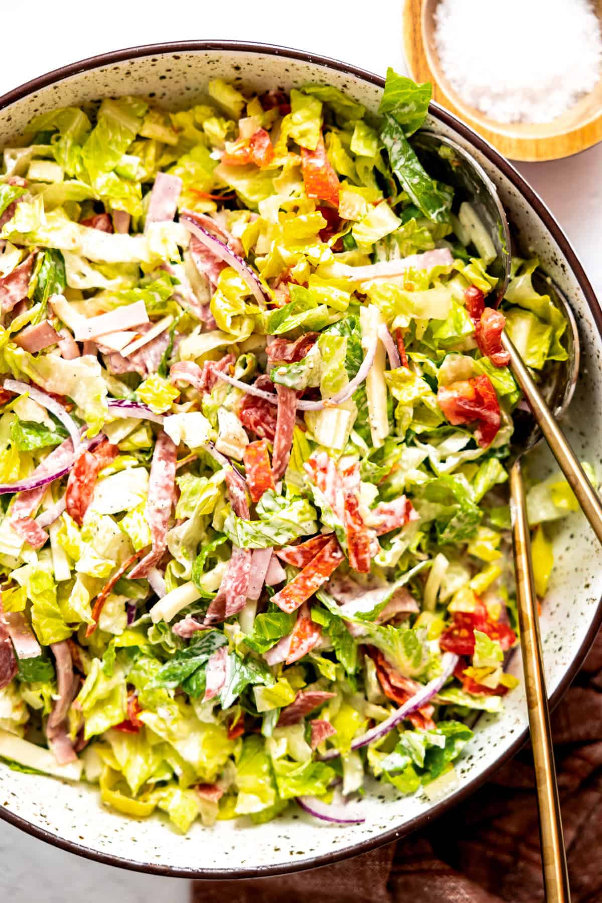 Tossed grinder salad in a bowl with serving spoons. 