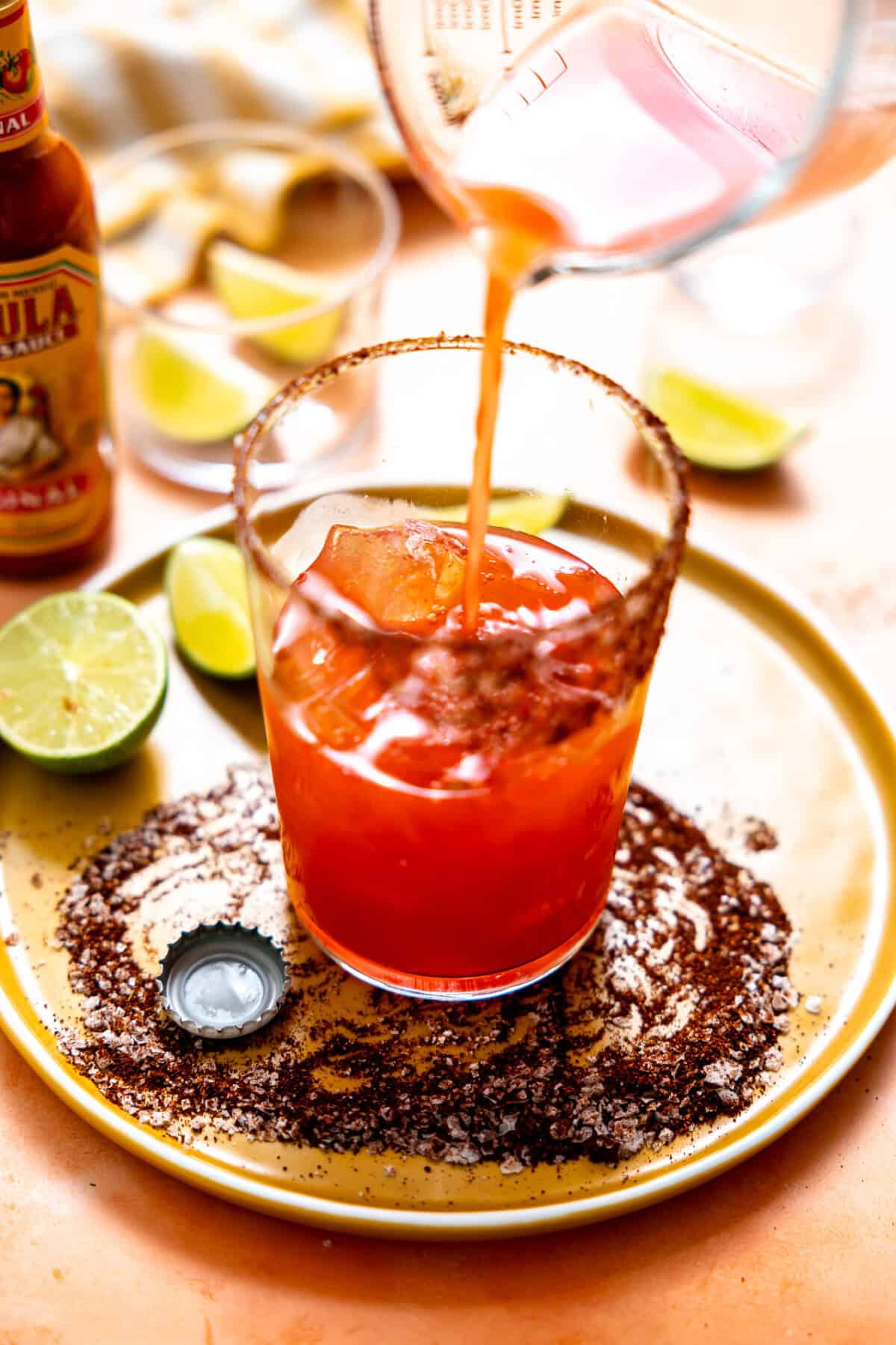 Pouring Clamato juice mixture into a glass for a Michelada. 