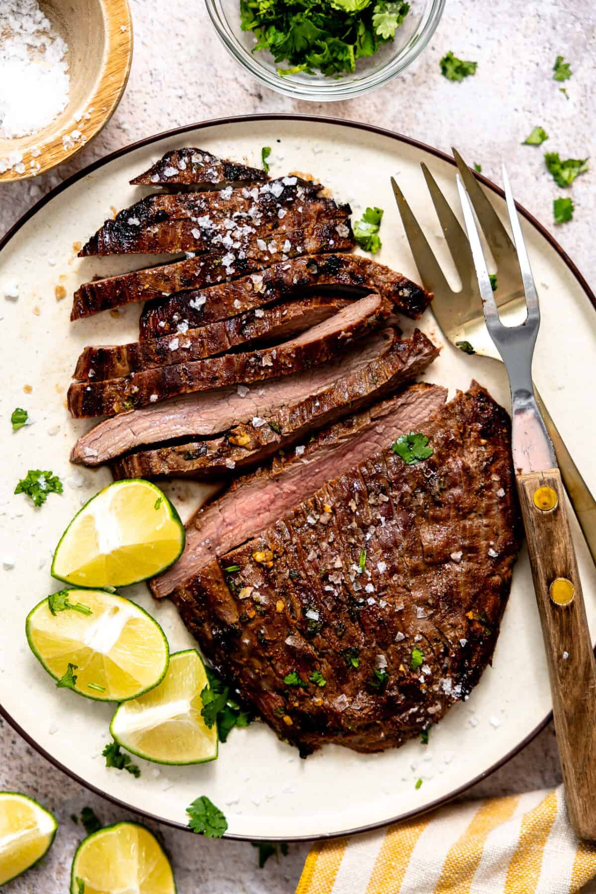 Plate filled with sliced carne asada with lime wedges on the side. 