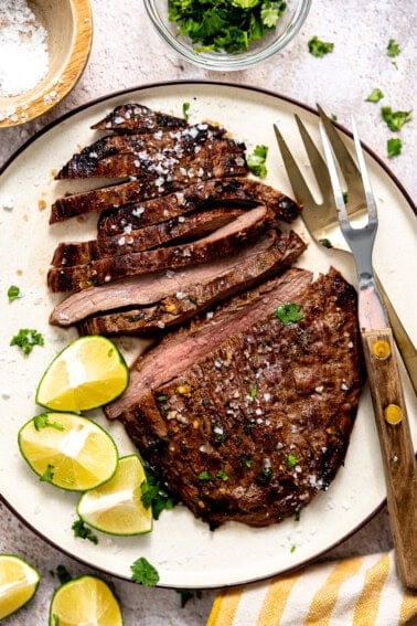 Plate filled with sliced carne asada with lime wedges on the side.