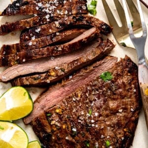 Sliced carne asada on a plate with lime wedges.